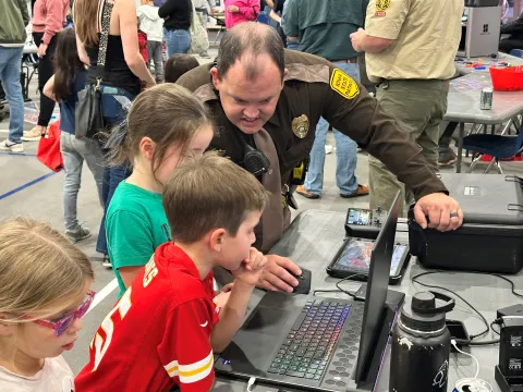 A sheriff shows three children a laptop.